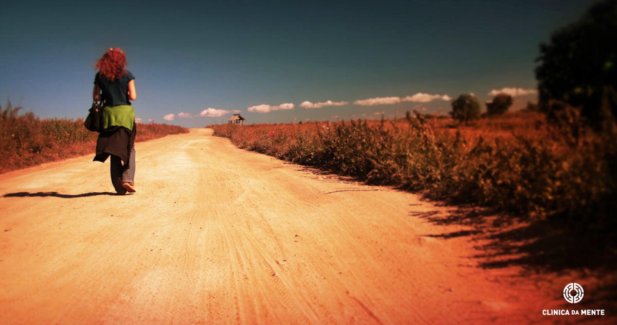 Mulher a caminhar por uma estrada de terra, simbolizando o sentimento de estar perdida e sozinha no sofrimento